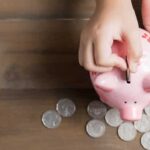 kid put coin to piggy bank on the vintage wood background